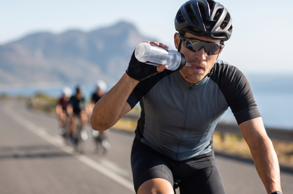 Ciclista em treino de endurance bebendo água durante prova, ilustrando a importância de hidratação e estratégia de reposição de fluidos em competições de longa duração